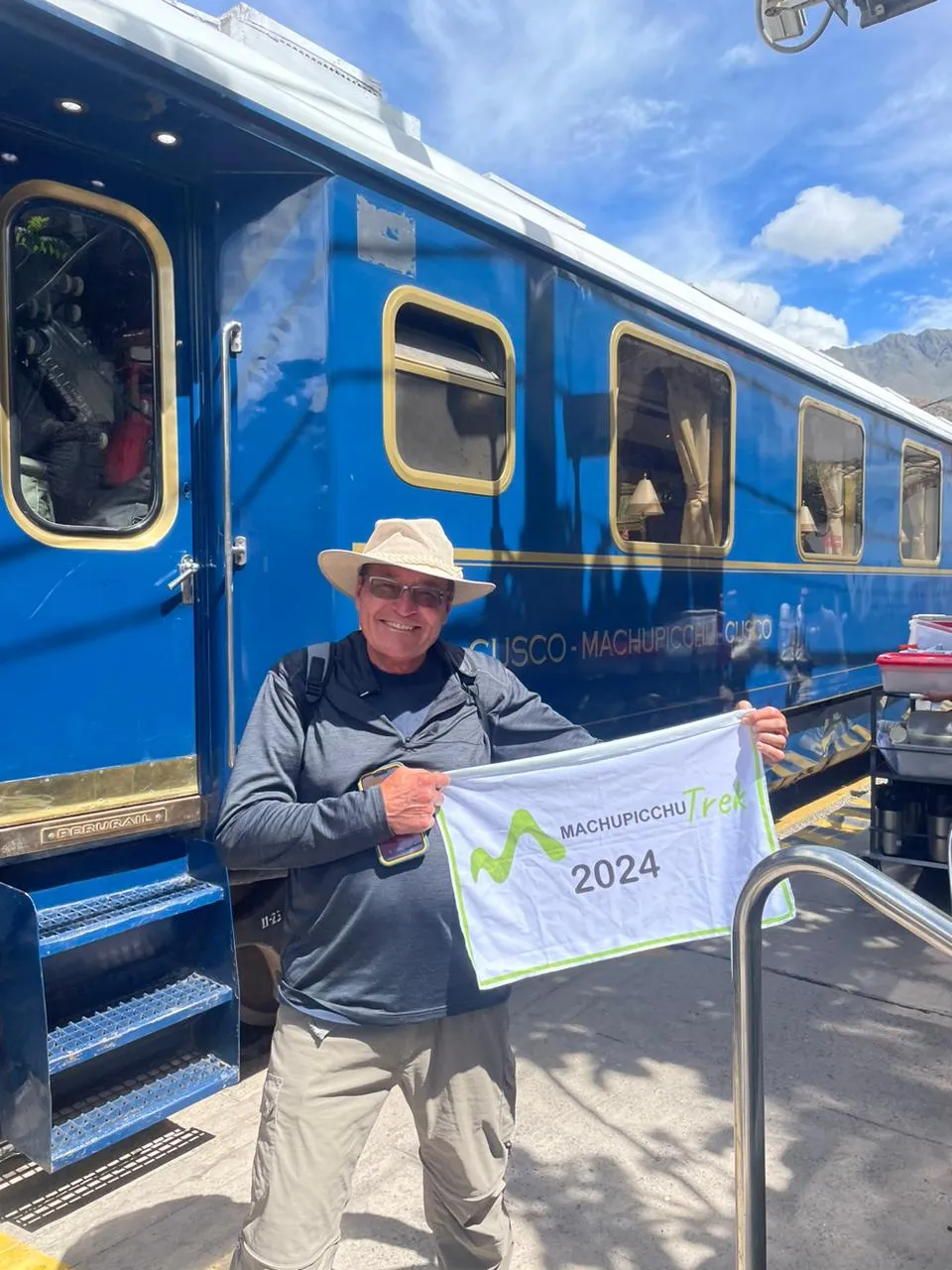 Man holding Machu Picchu Trek 2024 sign by train.