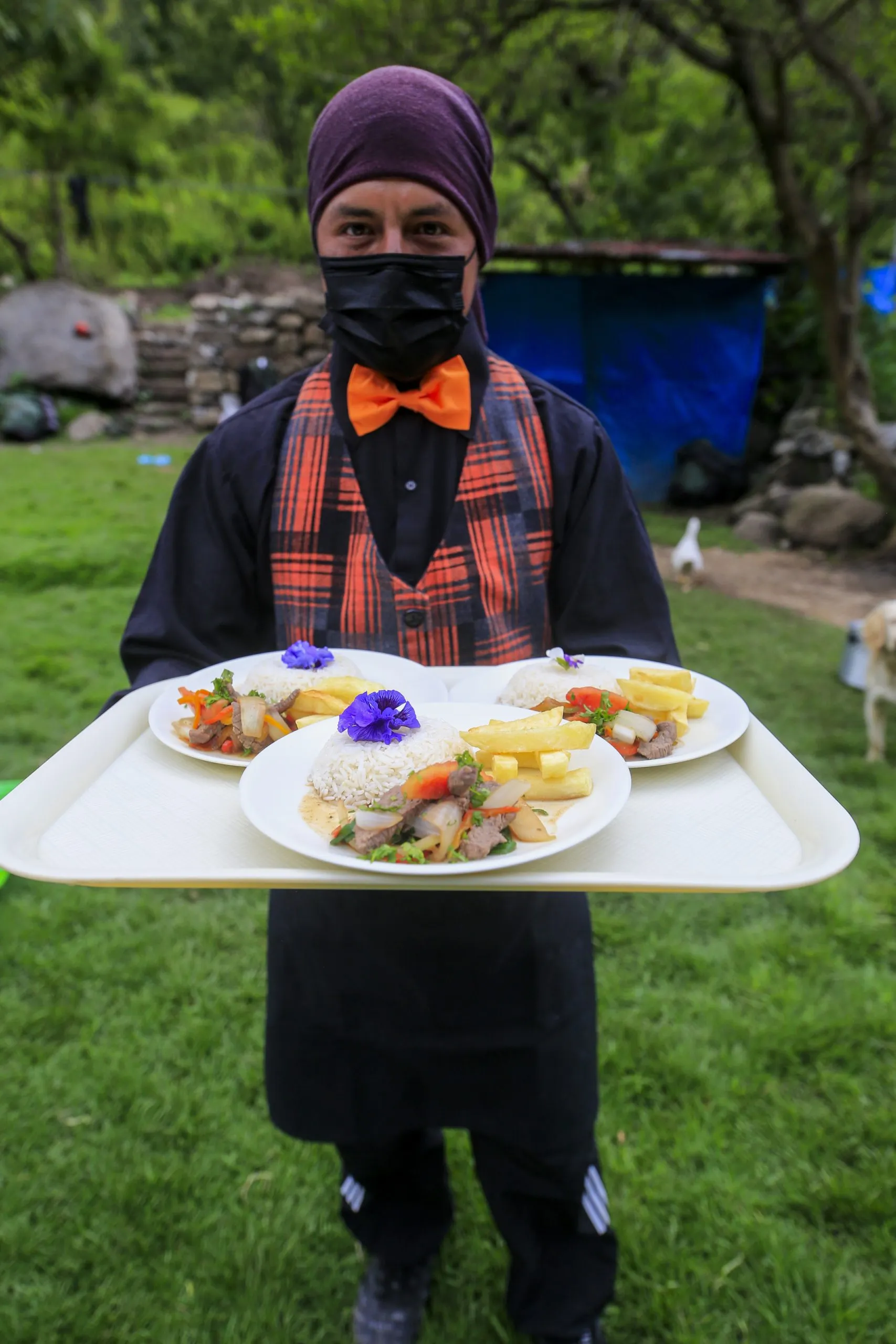 Waiter serves plated meals with flowers outside.