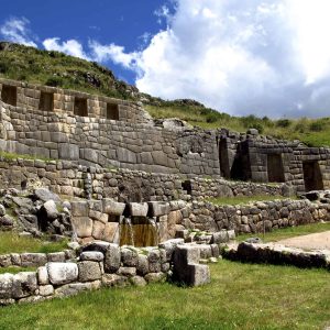 Ancient stone ruins with grassy landscape and blue sky.