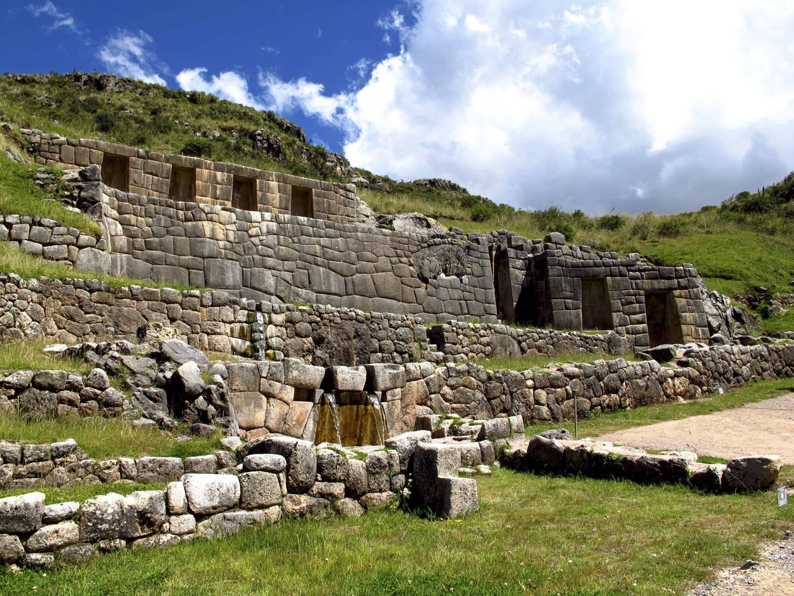 Ancient stone ruins with grassy landscape and blue sky.